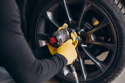 Mécanicien avec gants jaunes serrant les écrous d une jante de voiture à la clé à choc