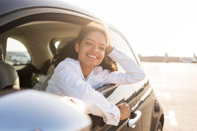 Jeune femme souriante à la fenêtre de sa voiture citadine au soleil