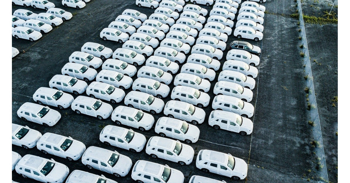 Vue aerienne de nombreux vehicules neufs blancs alignes sur un parc de stockage de flotte automobile