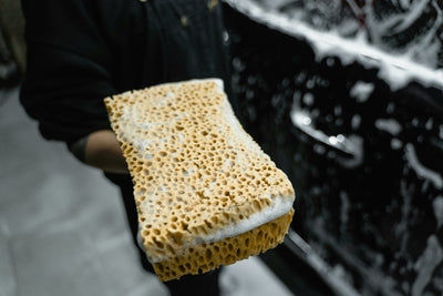 Une personne tient une éponge beige savonneuse pour le lavage et l entretien d un véhicule
