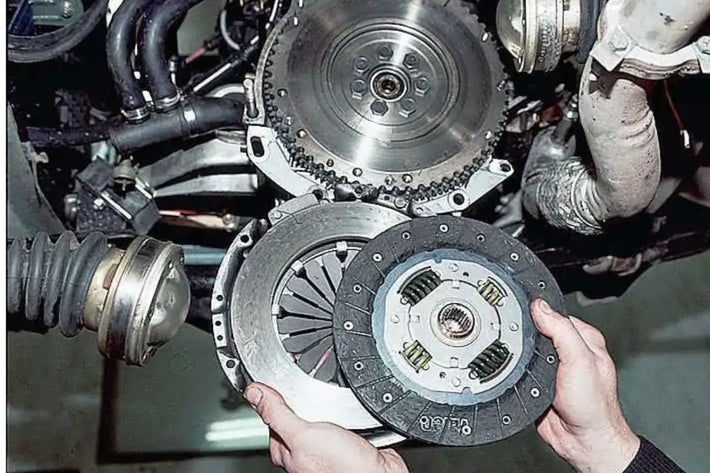 Mains d un mecanicien tenant un disque et un plateau d embrayage face au volant moteur