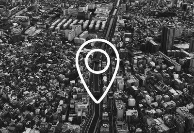 Icone de geolocalisation blanche survolant une vue aerienne de ville en noir et blanc pour localiser nos revendeurs