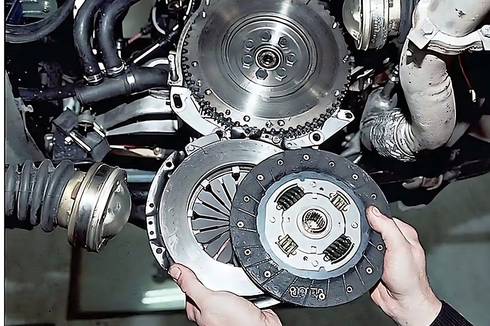 Mains d un mecanicien tenant un disque et un plateau d embrayage face au volant moteur