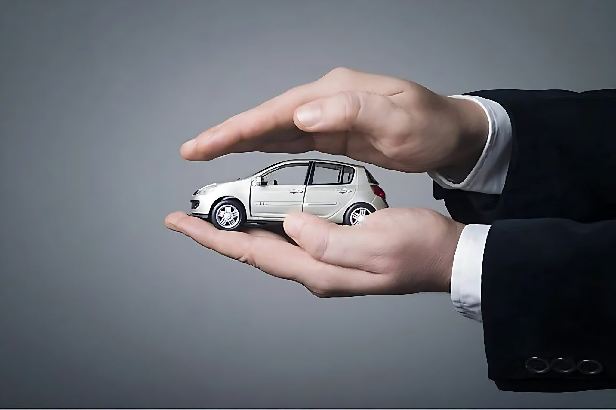 Mains de professionnel entourant une miniature de voiture grise pour choisir une assurance auto