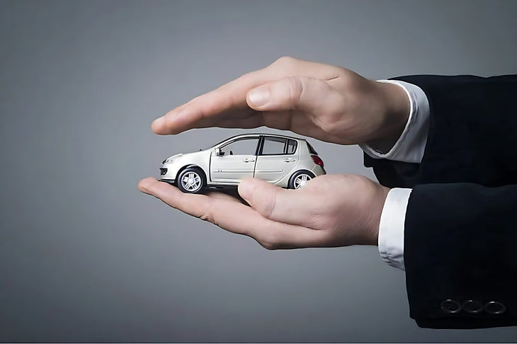 Mains de professionnel entourant une miniature de voiture grise pour choisir une assurance auto
