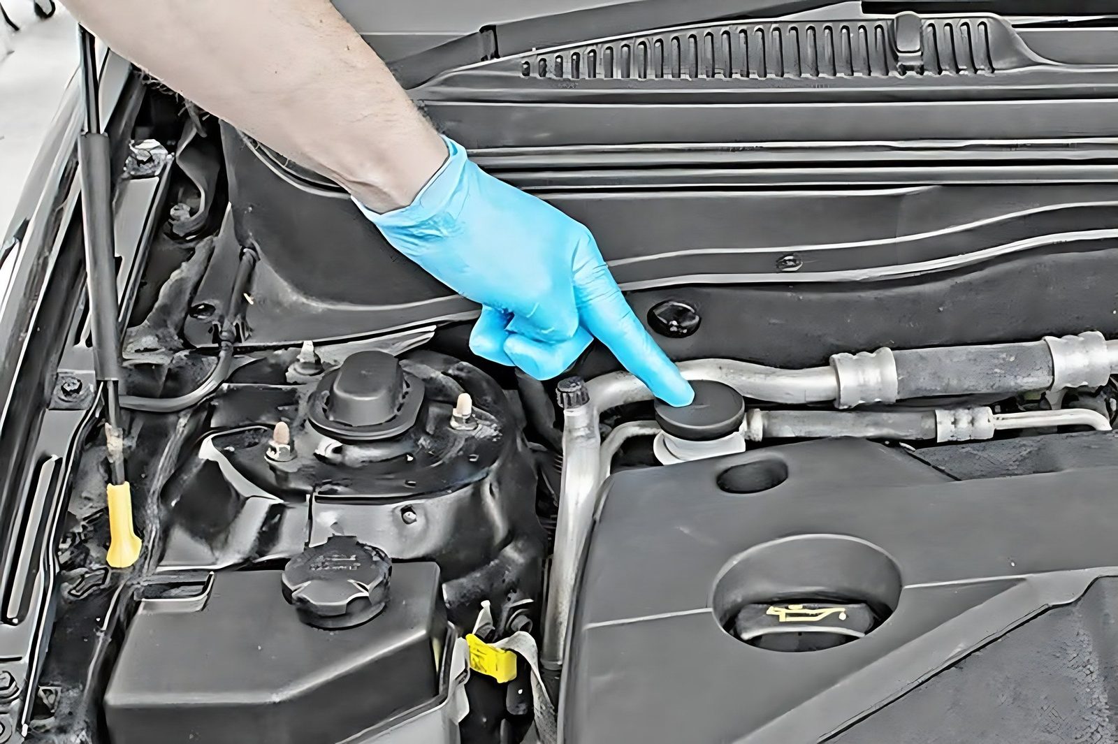 Un mecanicien avec gant bleu designe l emplacement du liquide d embrayage sous le capot