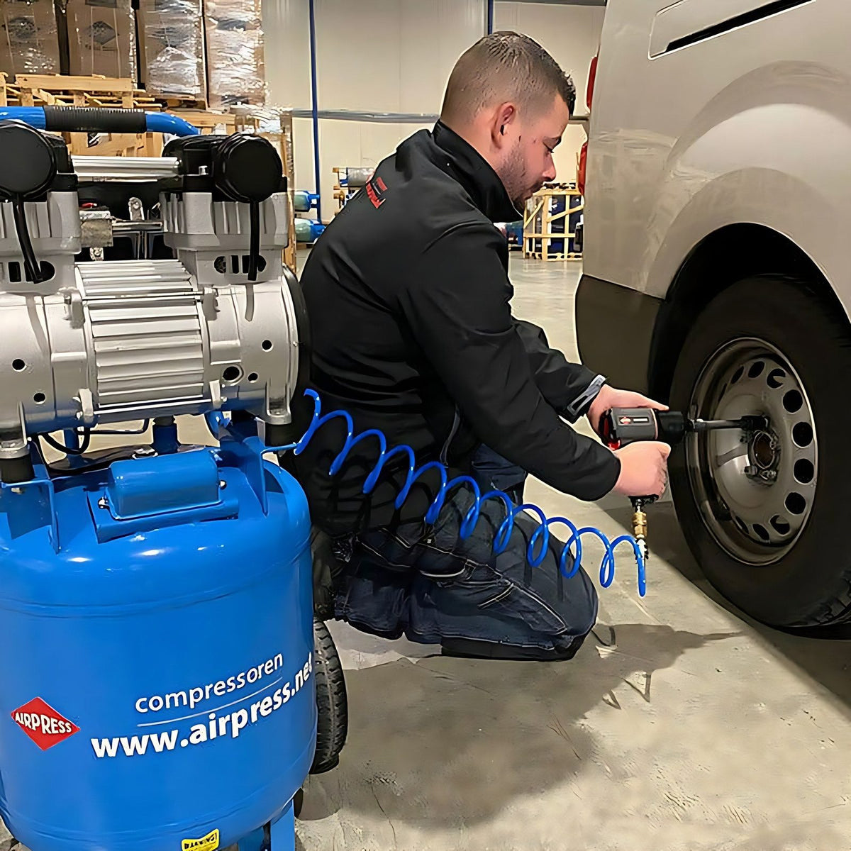 Technicien utilisant une cle a choc pneumatique reliee a un compresseur d atelier pour demonter une roue