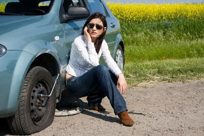 Femme au téléphone près d une voiture avec un pneu creve en panne sur la route