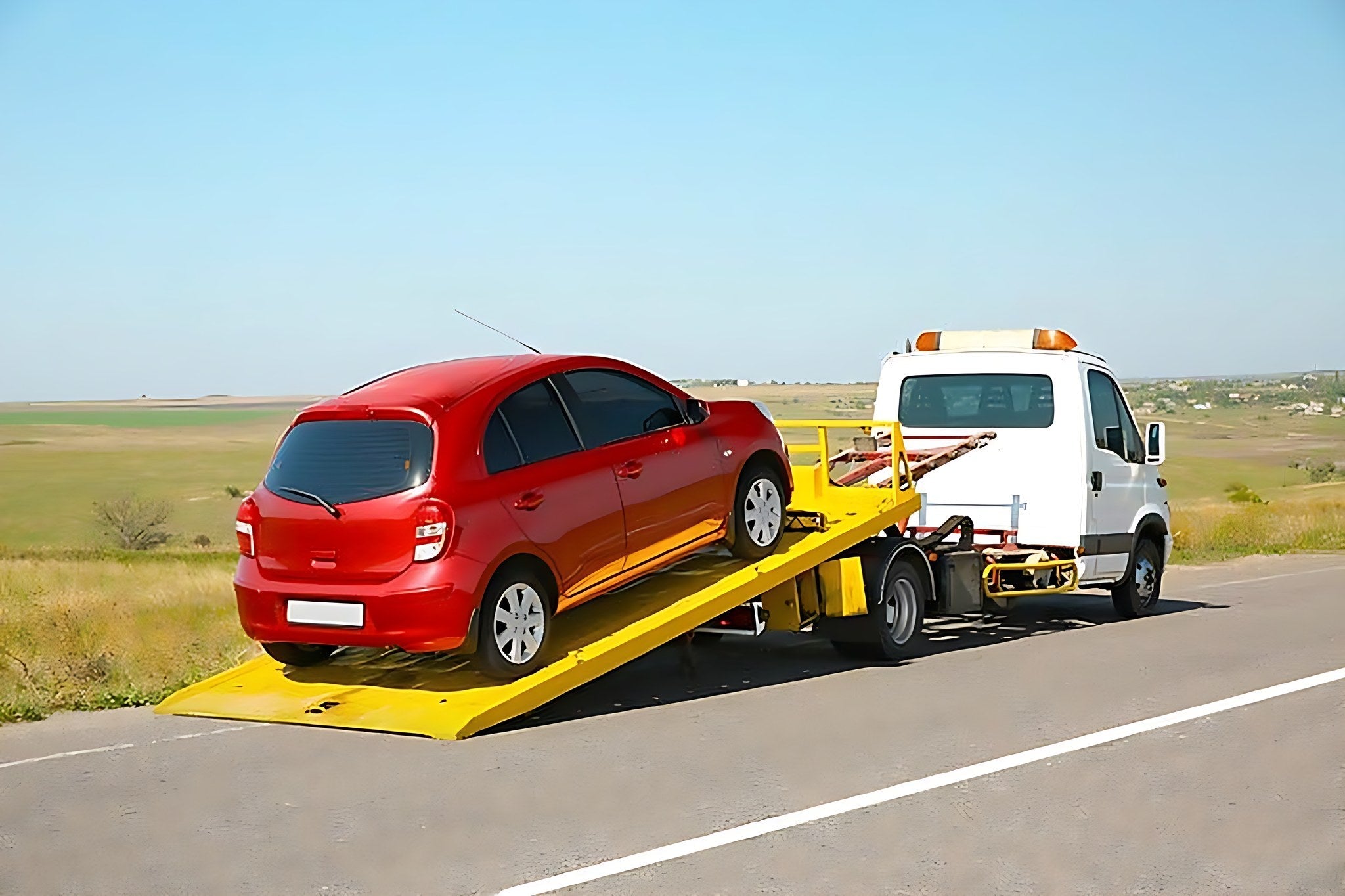 Voiture rouge en panne chargee sur une remorque depanneuse au bord de la route