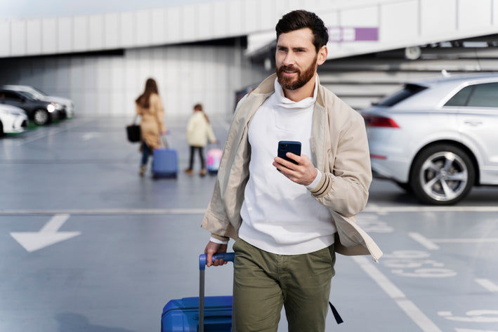 Homme avec smartphone et valise dans un parking d aeroport avant un diagnostic auto