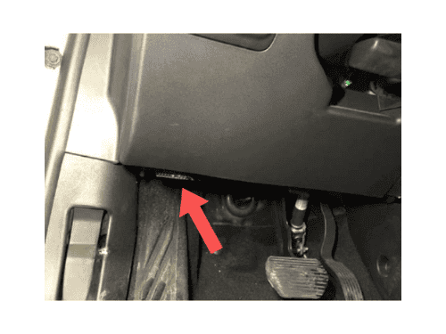Une flèche rouge indique l'emplacement de la prise OBD2 sous le tableau de bord d'une Citroën C3 Aircross