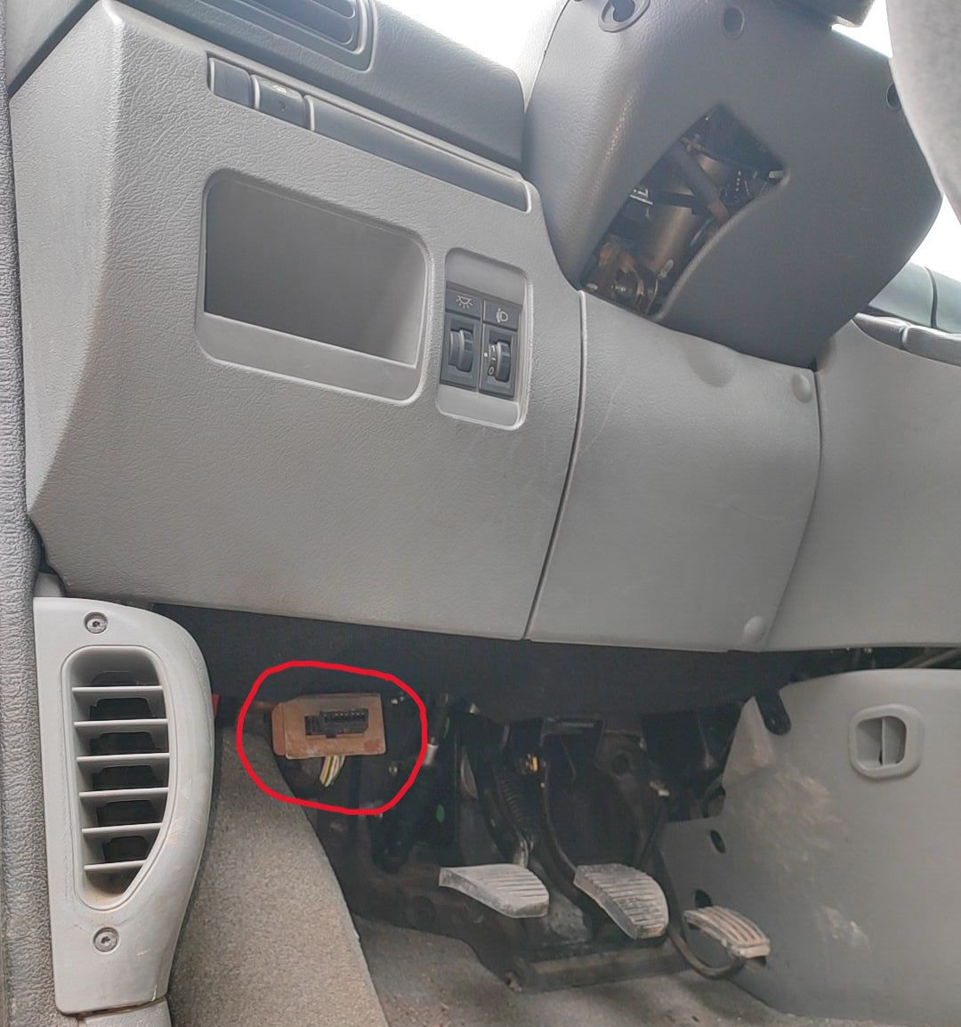 Prise de diagnostic OBD2 entouree en rouge sous le tableau de bord d une voiture