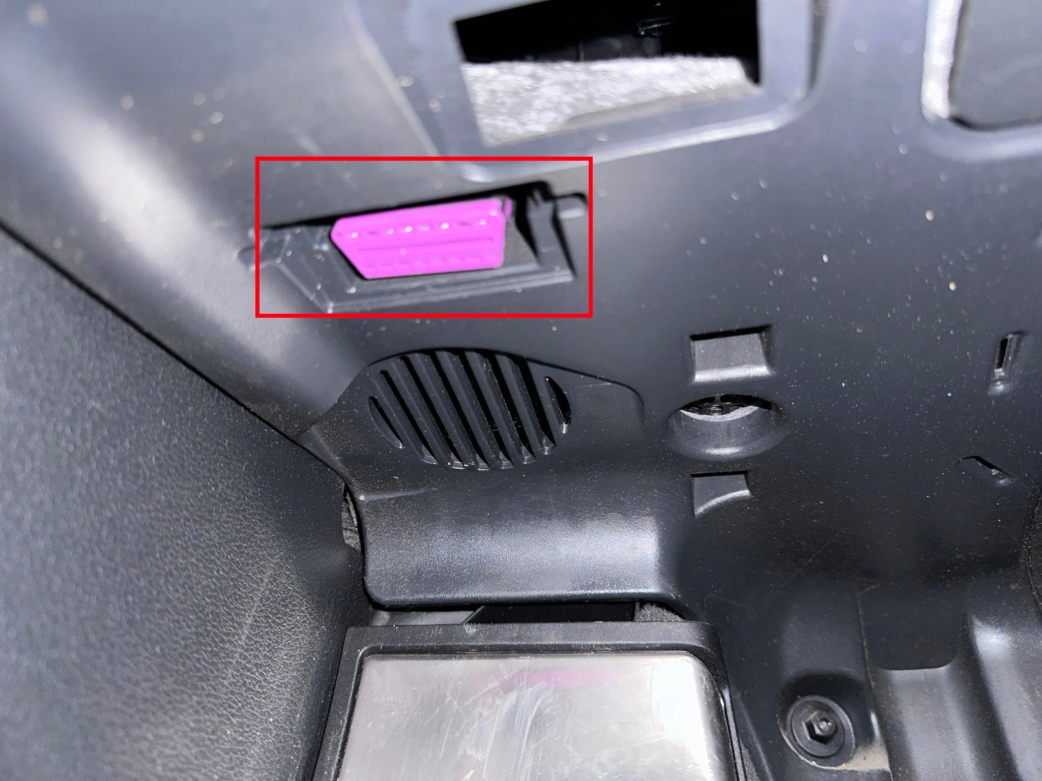 Prise de diagnostic OBD2 violette encadrée en rouge sous le tableau de bord d'un véhicule