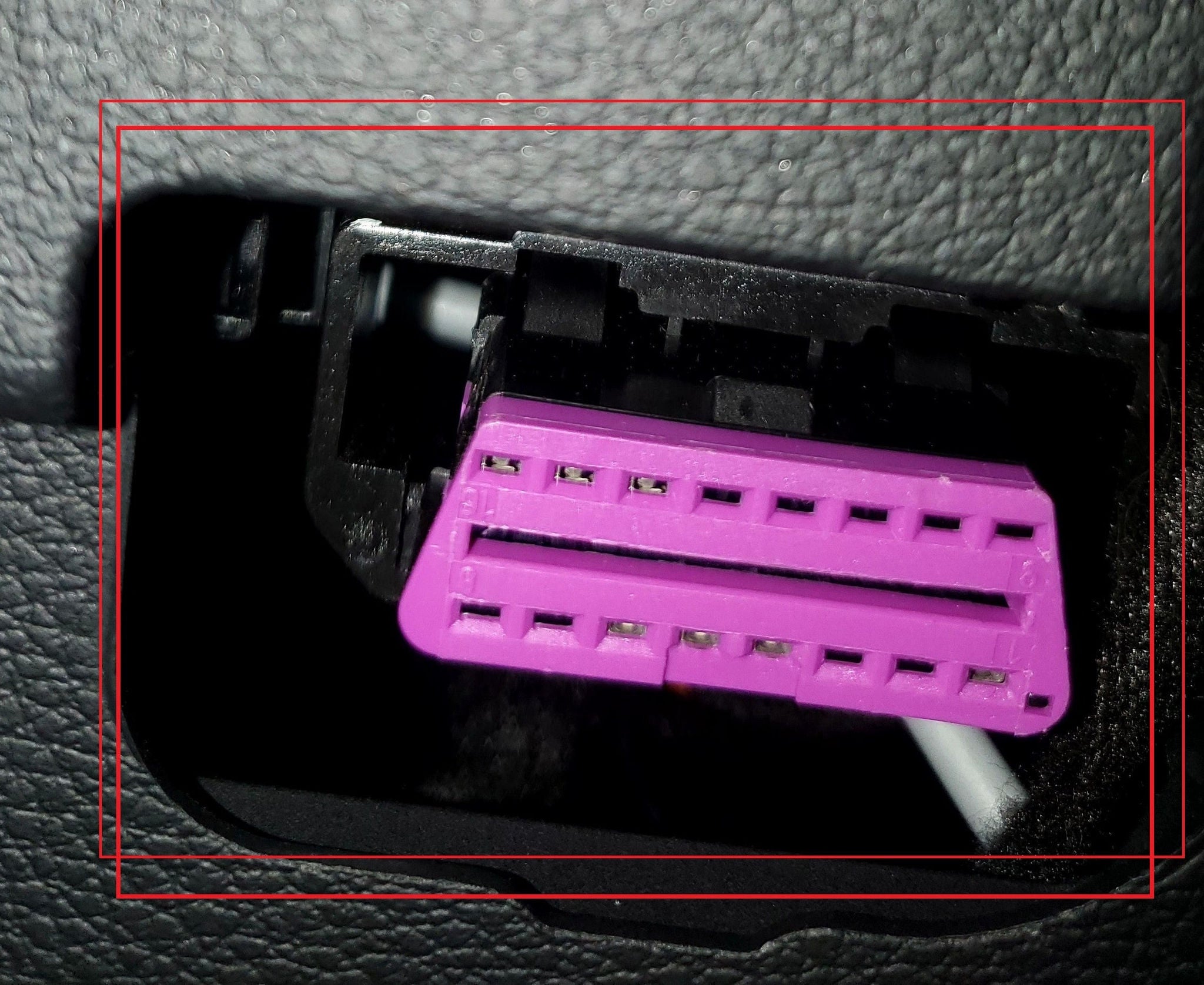 Gros plan sur la prise de diagnostic OBD2 violette sous le tableau de bord d'un véhicule