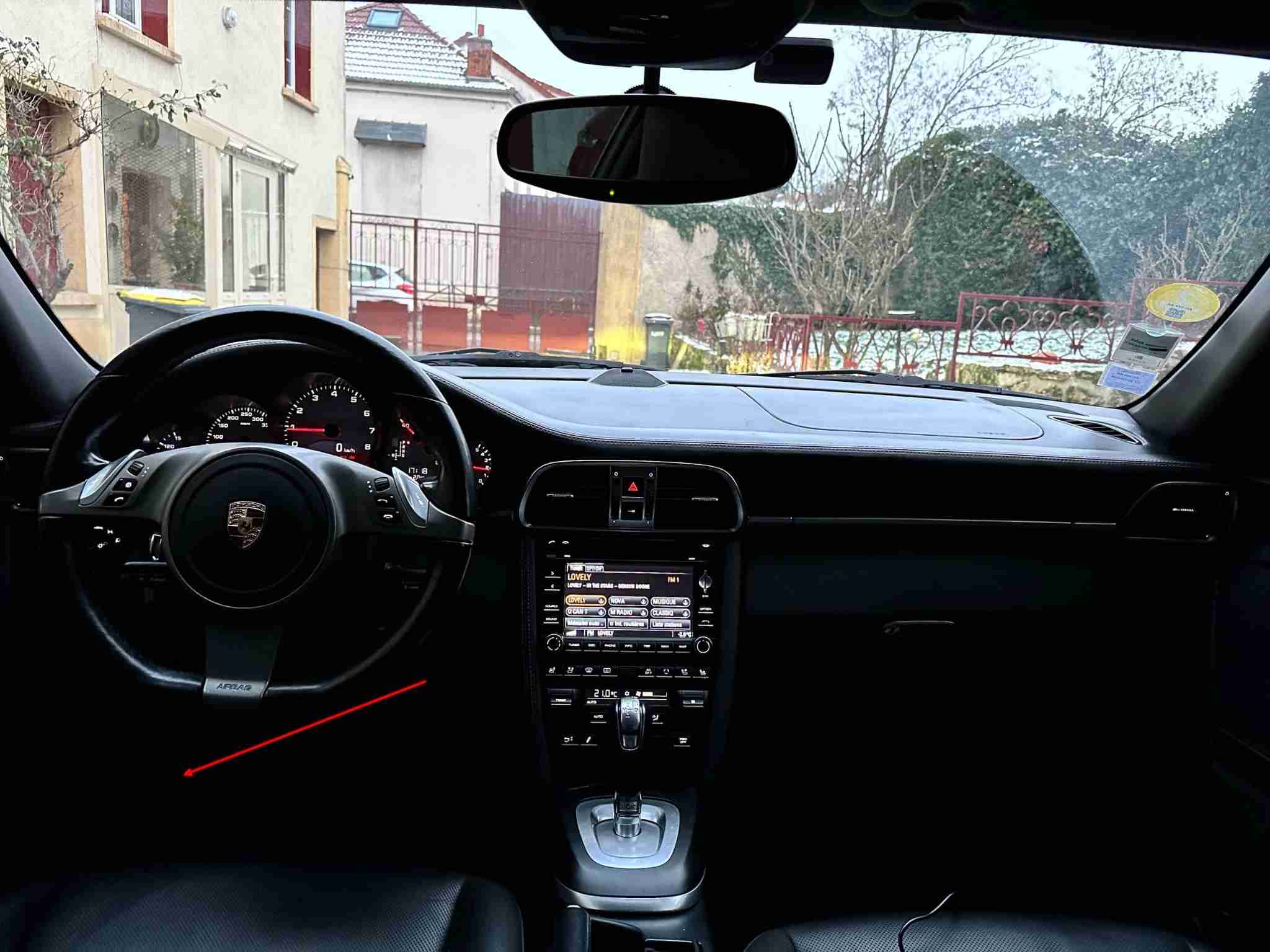 Vue intérieure de l'habitacle d'une Porsche avec une flèche rouge indiquant la prise OBD2