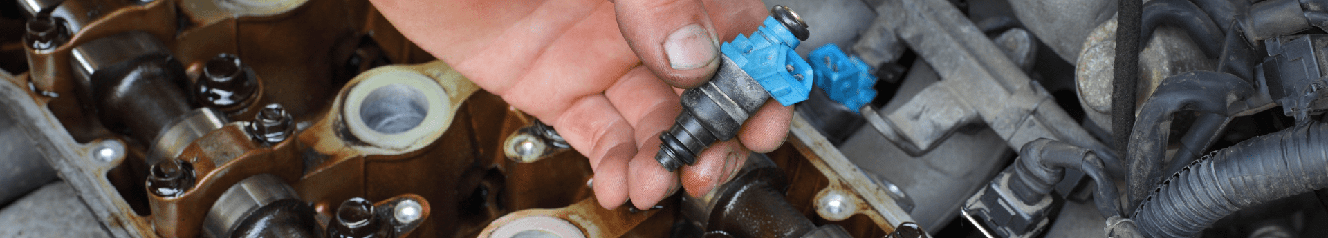 Un mécanicien tient un injecteur de carburant au-dessus d'un moteur de voiture ouvert